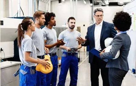 Un responsable en costume &eacute;change avec une &eacute;quipe d'ouvriers en bleu de travail dans une usine.