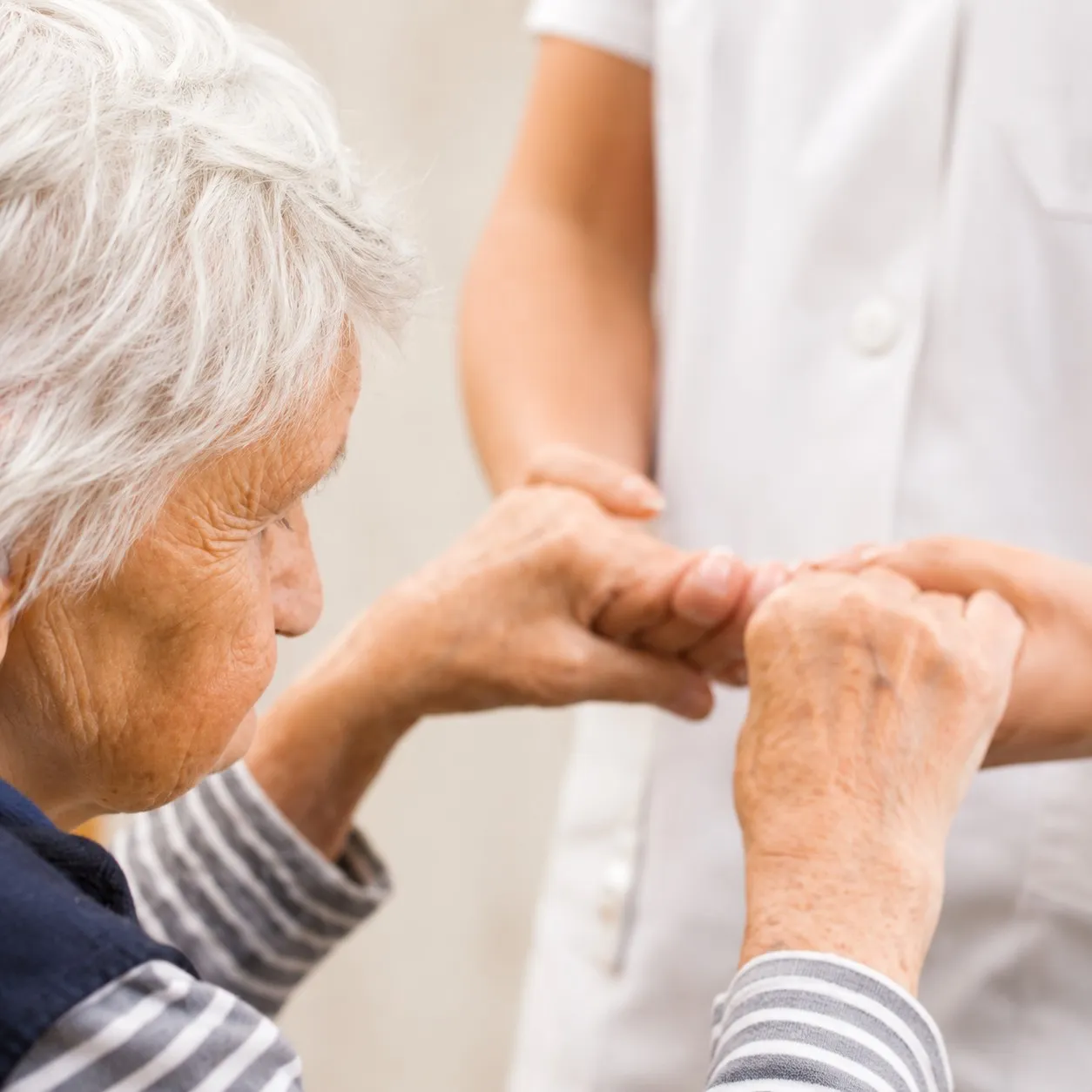 Une personne &acirc;g&eacute;e tient les mains d&rsquo;un membre du personnel soignant