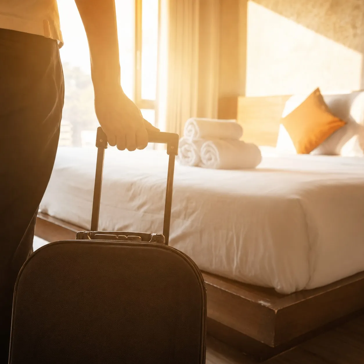 Une personne arrive dans une chambre d&rsquo;h&ocirc;tel avec une valise &agrave; roulettes